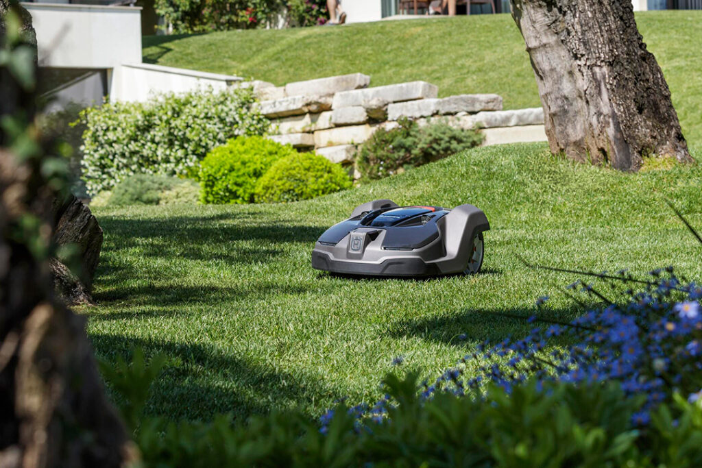 A Husqvarna 430x Automower driving through lush green lawns in a large garden.