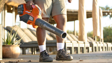 A man holding a Husqvarna battery-powered blower while removing leaves from his patio.