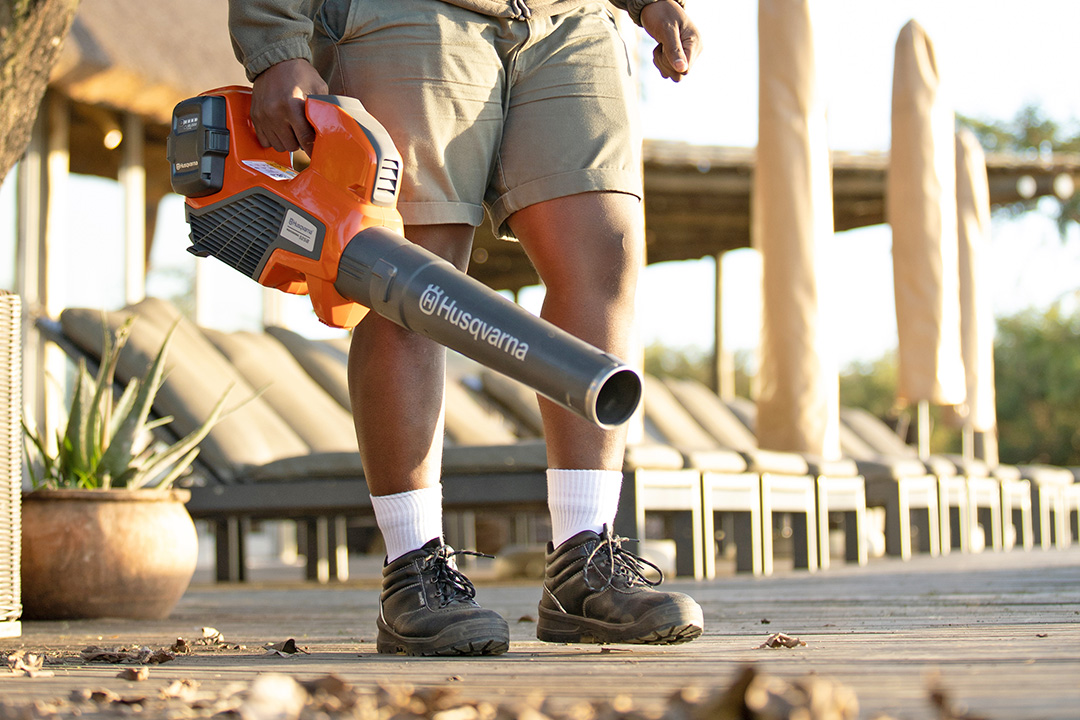 A man holding a Husqvarna battery-powered blower while removing leaves from his patio.