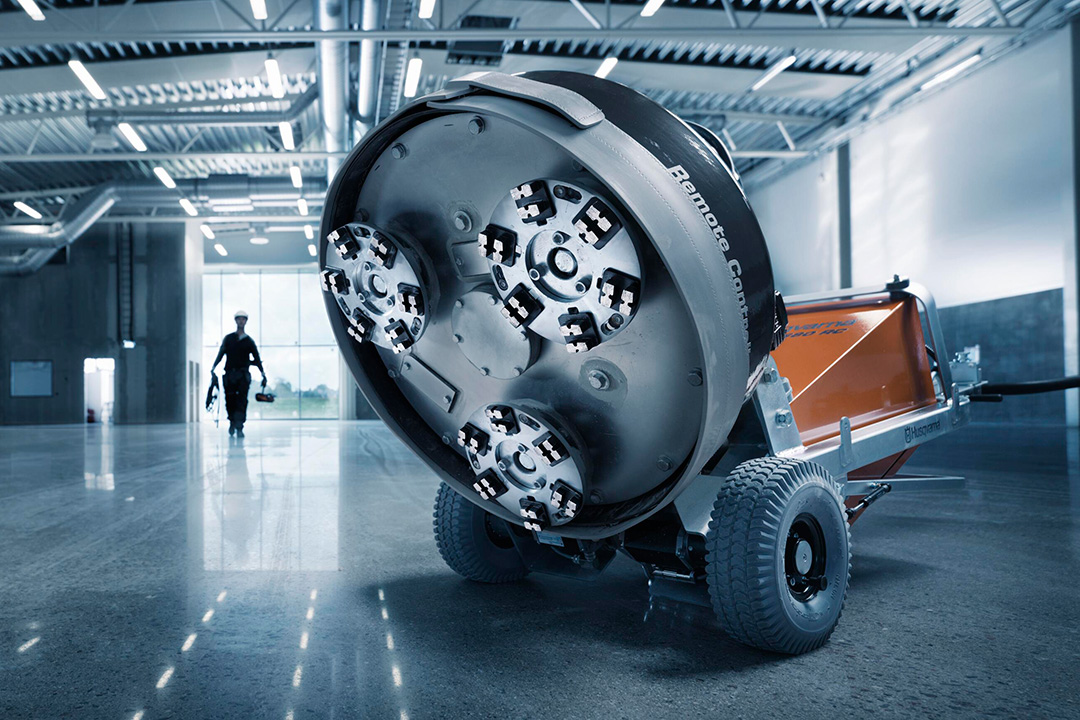 The underside of a Husqvarna concrete polisher on a shiny concrete floor in a warehouse.