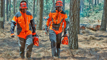 A forester wearing safety gear cuts the branches off a fallen tree with a Husqvarna chainsaw