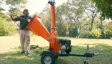 A man feeds a branch into a Hunter wood chipper on wheels.