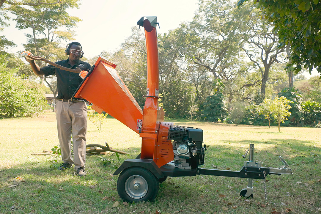 A man feeds a branch into a Hunter wood chipper on wheels.