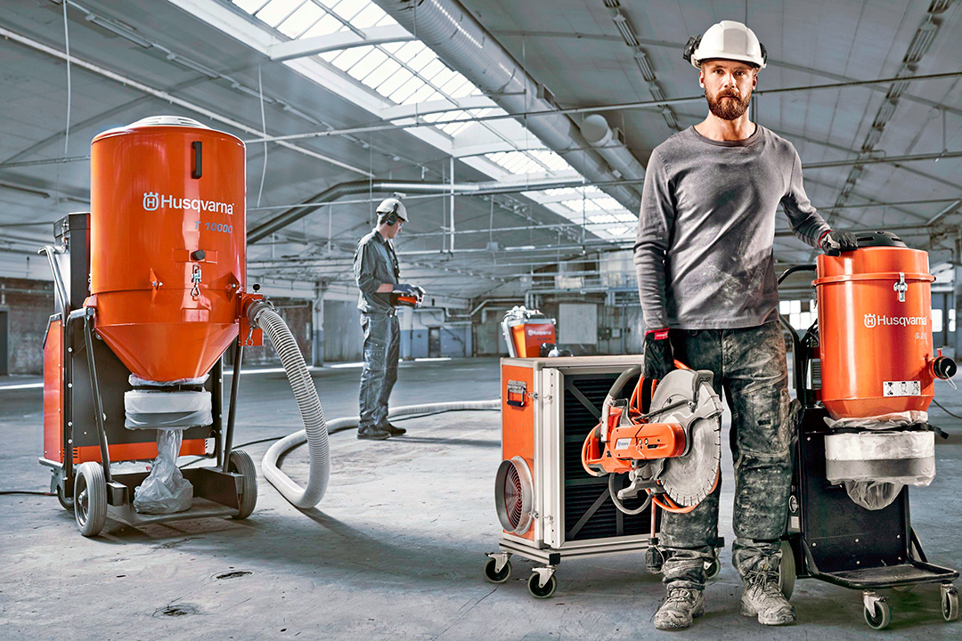 A construction worker standing inside a warehouse next to some Husqvarna dust extraction machines.