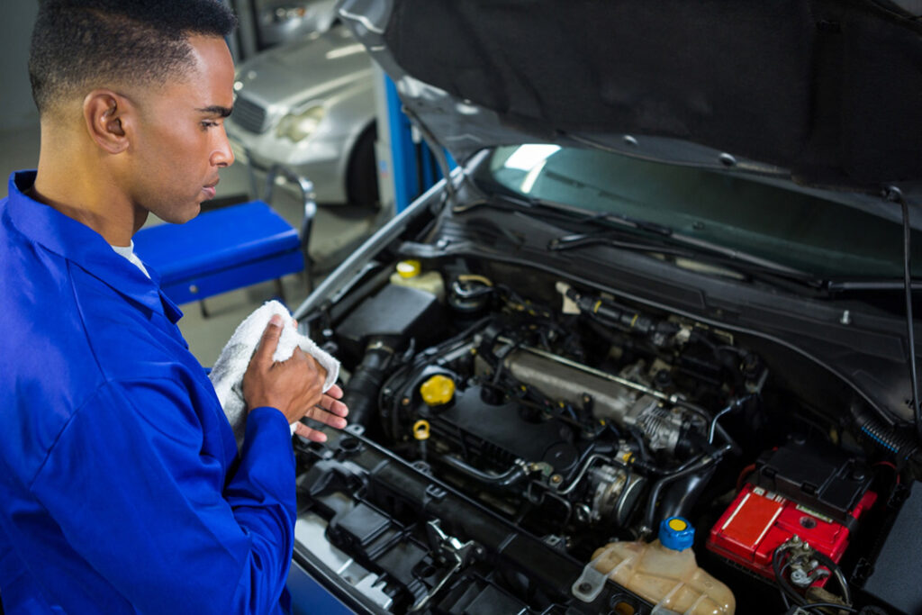 A mechanic wipes his hands after fixing the engine of small car.