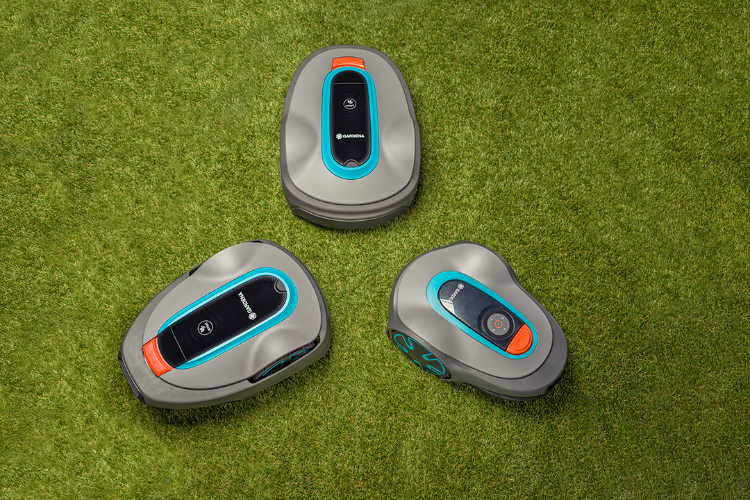 Three GARDENA robotic mowers in a triangle on a green lawn.