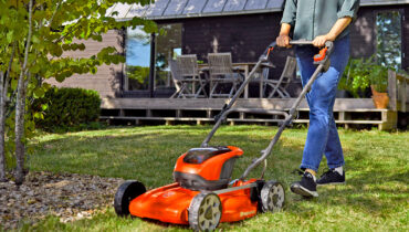 A Husqvarna LB144i battery mower being pushed across lush green lawn.