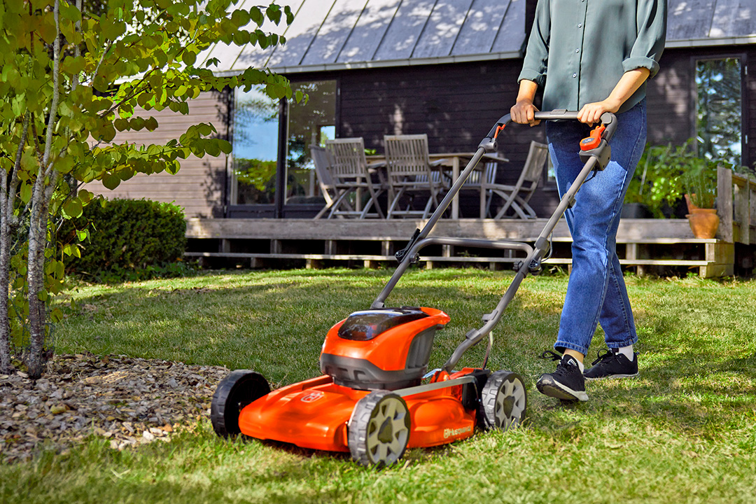 A Husqvarna LB144i battery mower being pushed across lush green lawn.