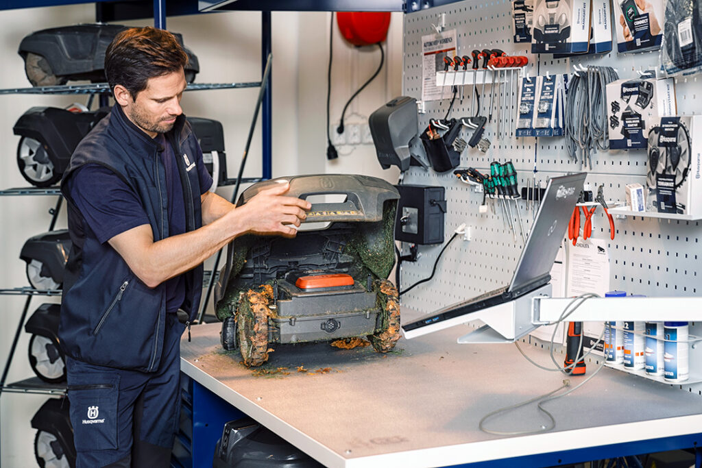 A man servicing a Husqvarna 430 Automower in a workshop.