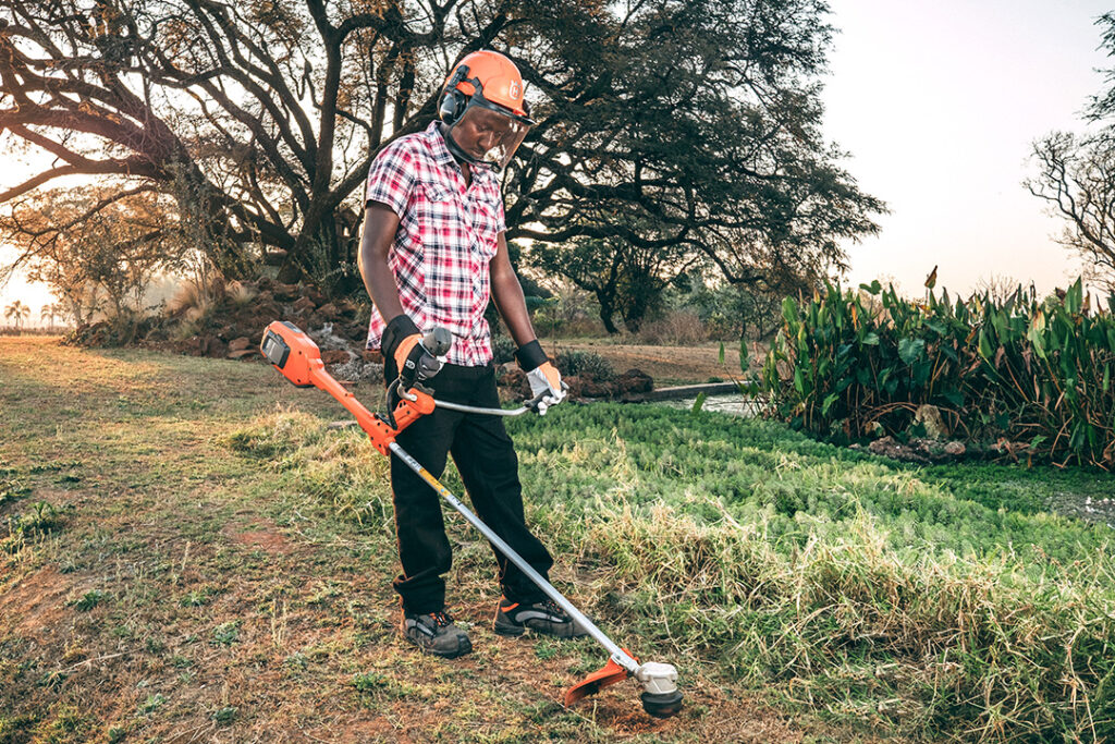 A man holds a Husqvarna battery brushcutter next to a garden dam in Zimbabwe.