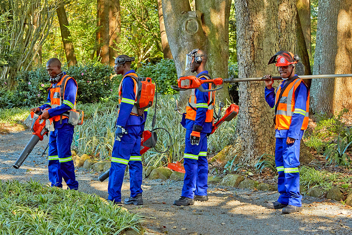 A team of workers holding Husqvarna battery equipment in a lush garden.