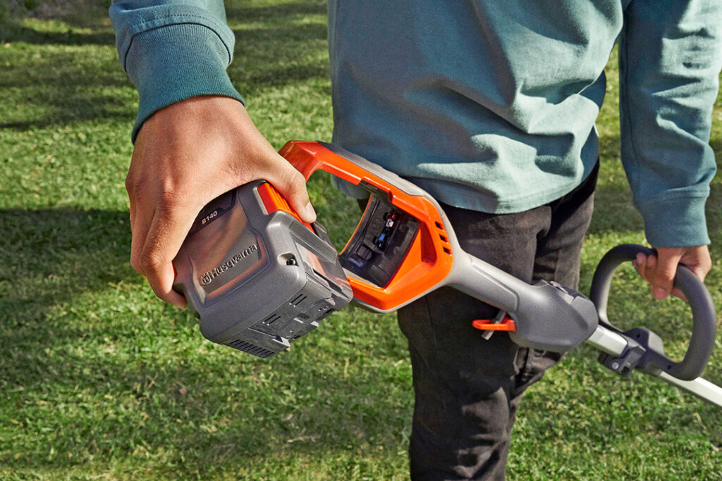 A close-up photo of a Husqvarna battery being inserted into a brushcutter.