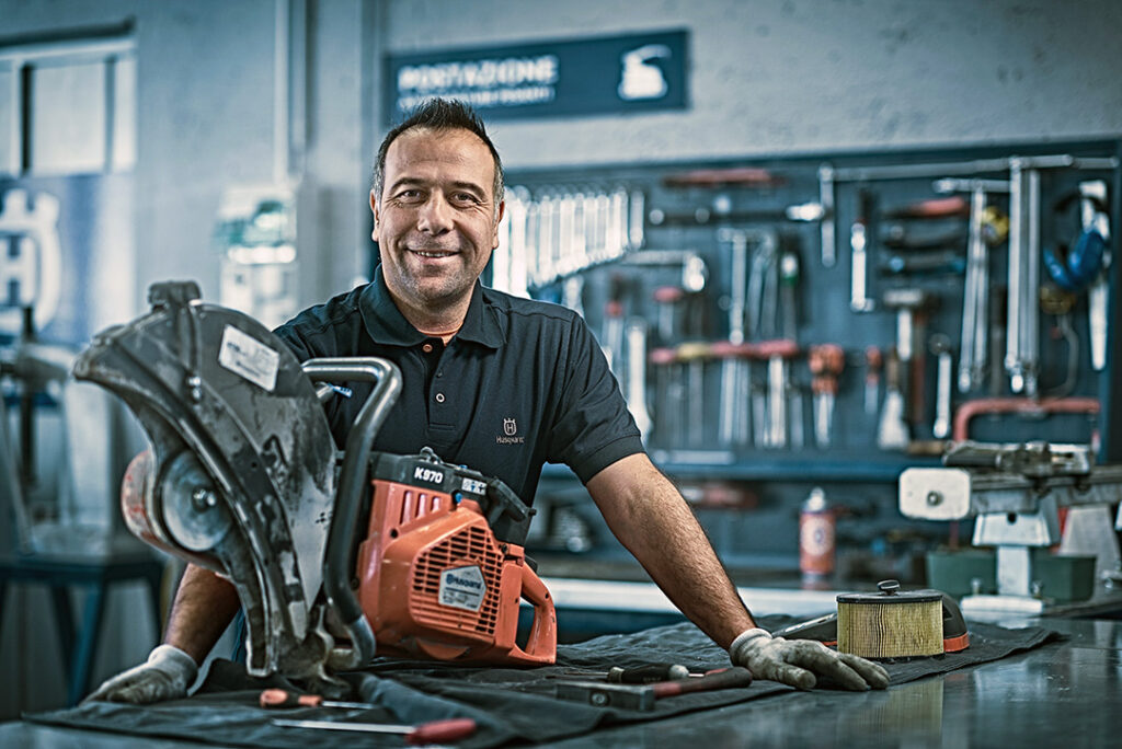 A mechanic smiles while working on a Husqvarna power cutter inside his workshop.