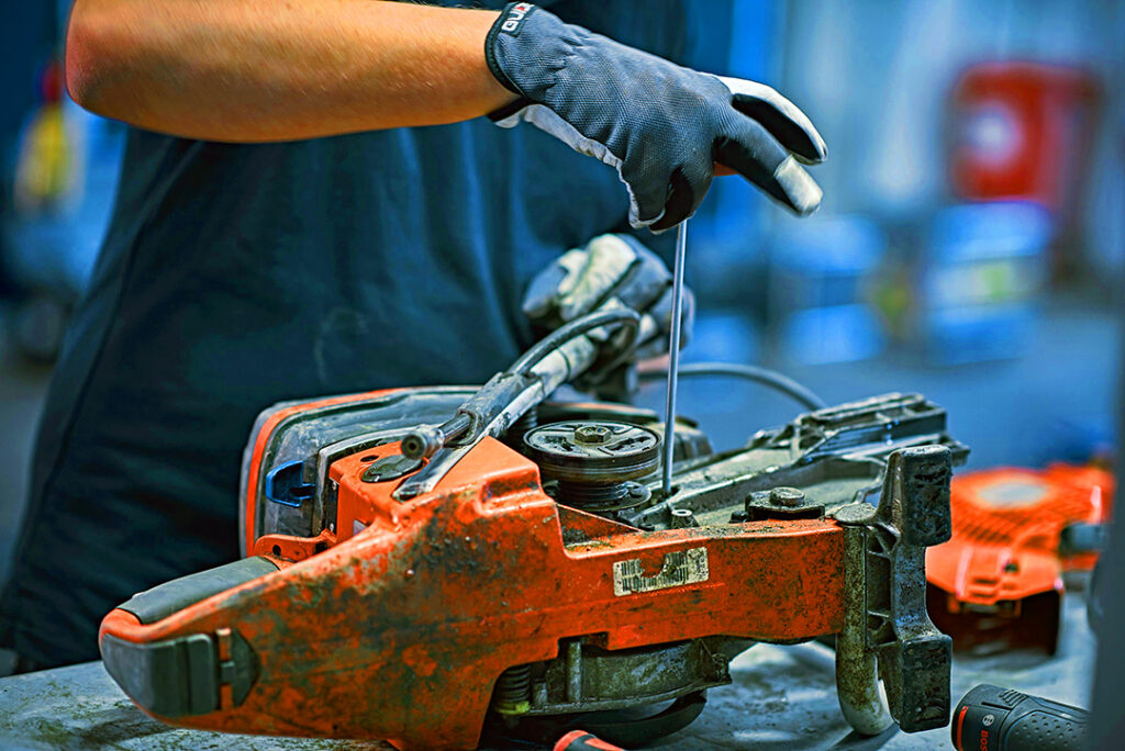 A mechanic servicing a Husqvarna power cutter on a work bench.