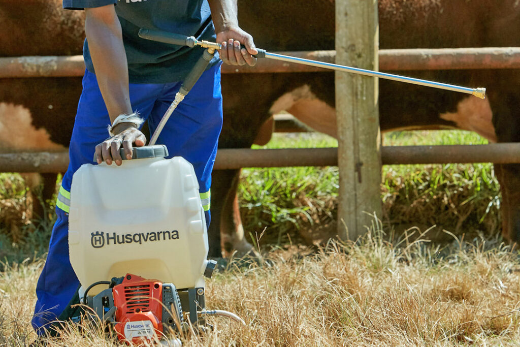 A close-up of a Husqvarna sprayer being used to treat cattle with anti-tick medicine.