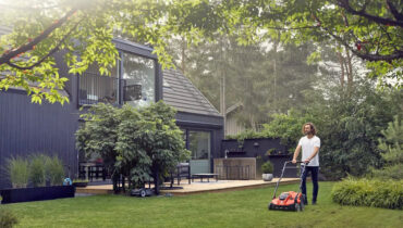 A man pushing a Husqvarna scarifier across green lawn in front of his house.