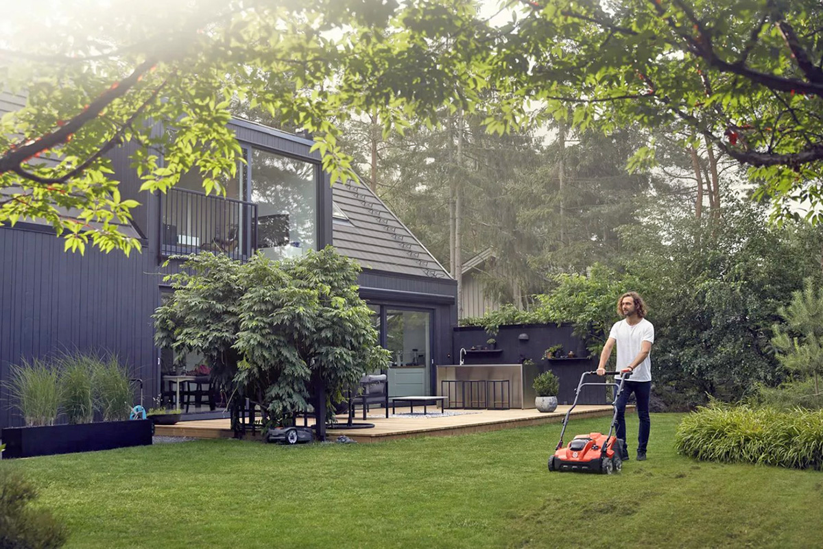 A man pushing a Husqvarna scarifier across green lawn in front of his house.