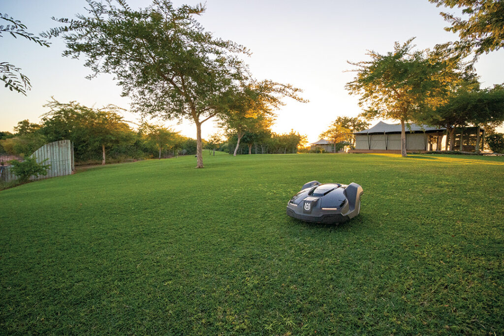 A Husqvarna Automower on a lush green lawn at sunset in Kariba.