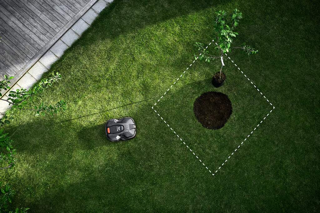 An aerial view of a Husqvarna Automower on a green lawn with an imaginary boundary around a tree.